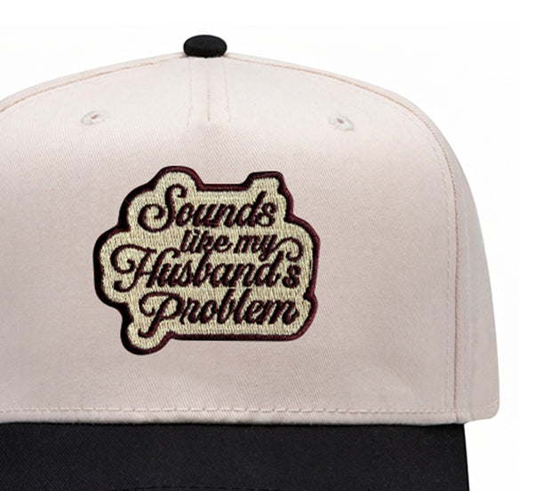 Close-up of the Sounds Like My Husband's Problem embroidered patch on a black trucker hat