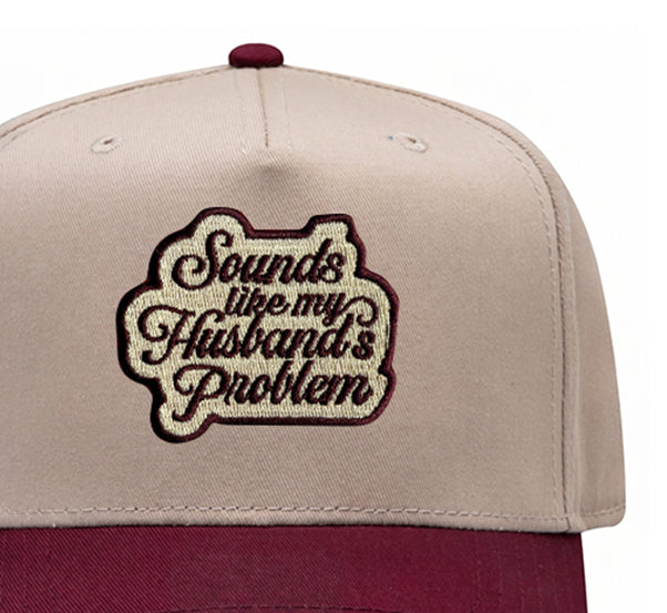 Close-up of the Sounds Like My Husband's Problem embroidered patch on a maroon trucker hat