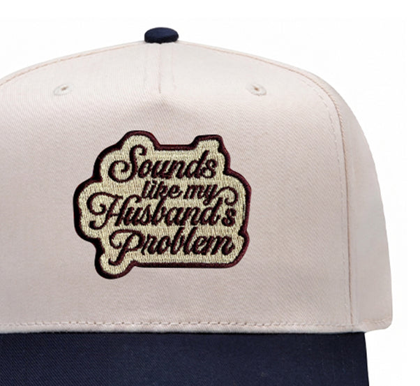 Close-up of the Sounds Like My Husband's Problem embroidered patch on a navy trucker hat