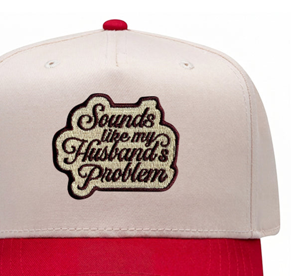 Close-up of the Sounds Like My Husband's Problem embroidered patch on a red trucker hat