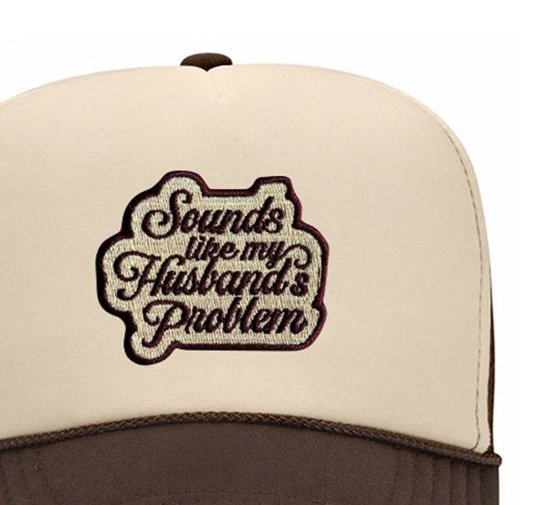 Close-up of the Sounds Like My Husband's Problem embroidered patch on a tan and brown trucker hat